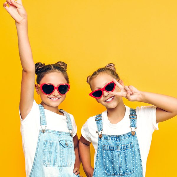 Two teenage girls, stylish girlfriends posing on a yellow background showing two fingers